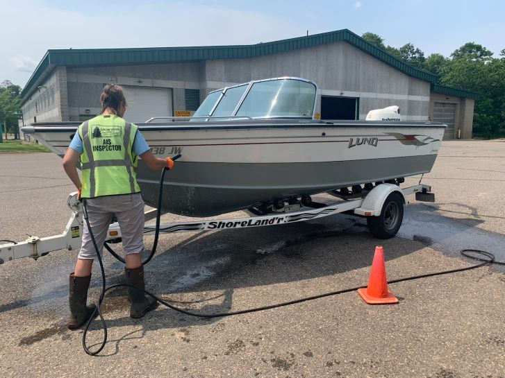 A Person with a yellow vest sprays off a fishing boat on a sunny day